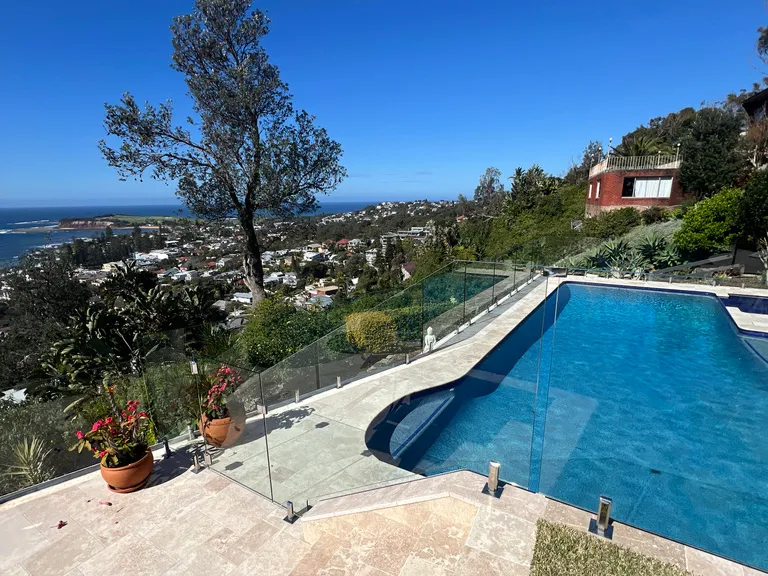 Pool behind a frameless glass fence on a hillside, looking out to the ocean