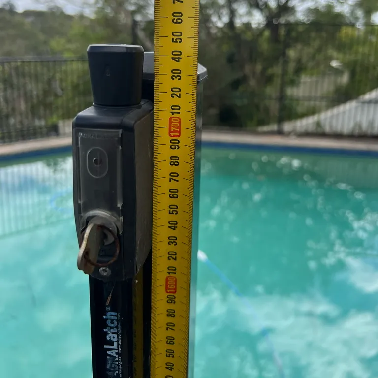 Close-up of a pool gate latch with a tape measure beside it