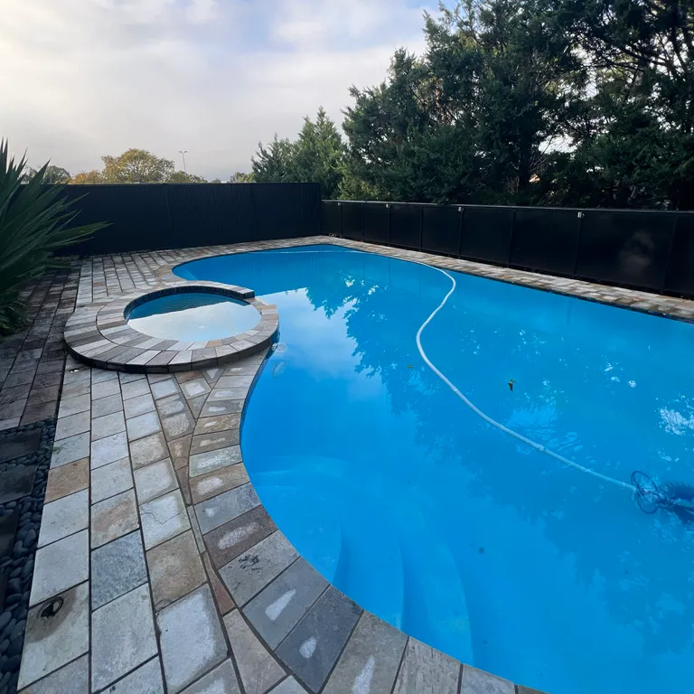 Kidney-shaped pool and spa with stone paving and a dark fence along the back of the yard